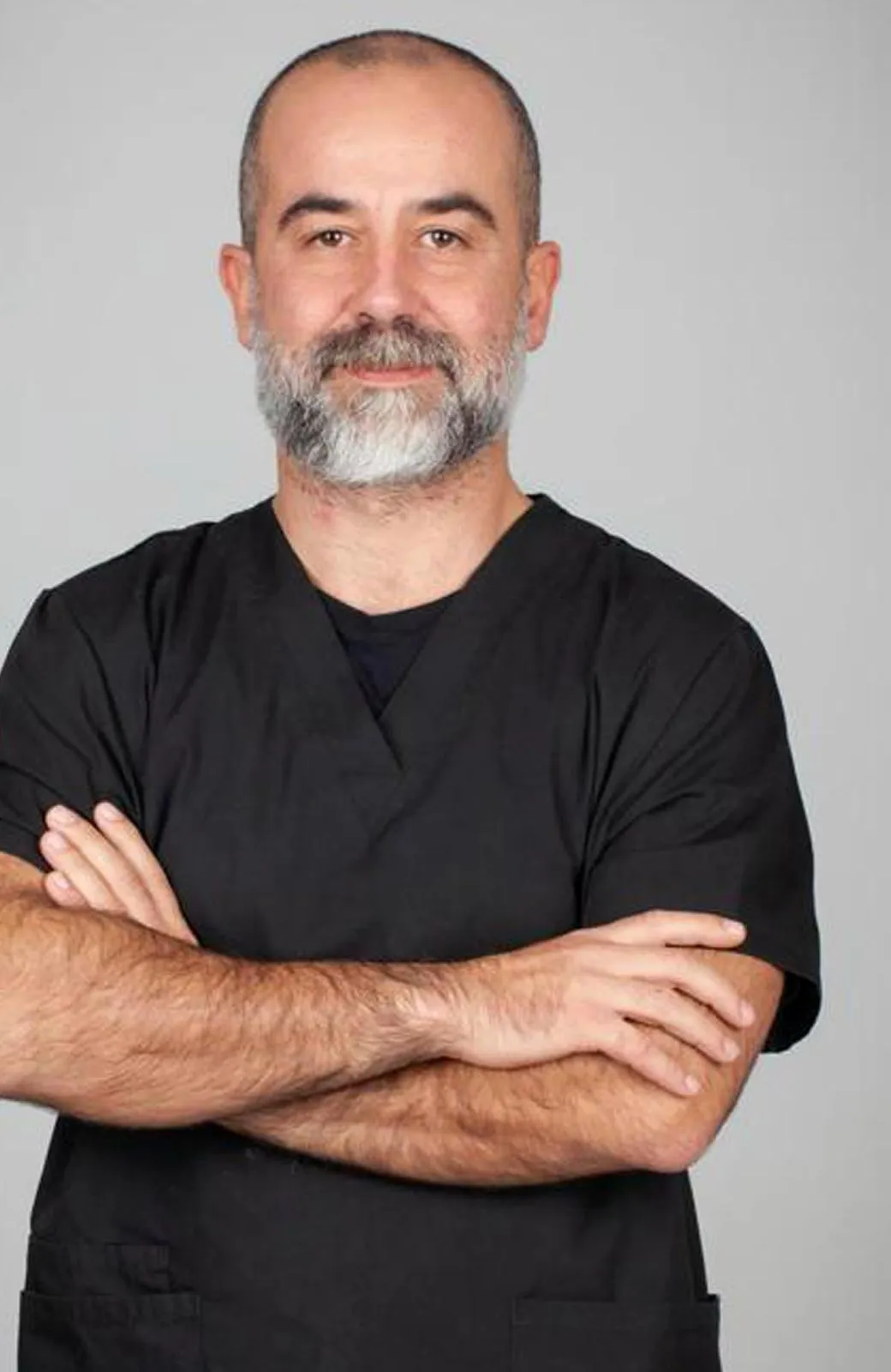 Il Dott. Pierfrancesco Cadenelli in camice nero, braccia conserte, nello studio